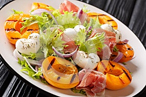 Easy dietary salad with mozzarella, prosciutto, grilled apricots, red onion and lettuce close-up on a plate. horizontal