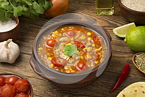 Easy Mexican chicken and rice soup in a terracotta soup bowl on a rustic wooden table with ingredients.