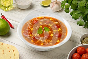 Easy Mexican chicken and rice soup in a white soup bowl on a rustic white table with ingredients.