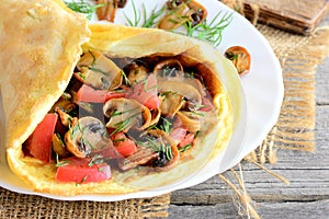 Easy mushrooms omelet recipe. Homemade omelette stuffed with mushrooms, tomatoes and dill on a plate and old wooden background