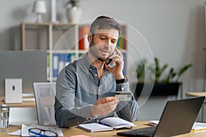 Easy payments concept. Mature businessman worker holding credit card and talking on cellphone with customer service