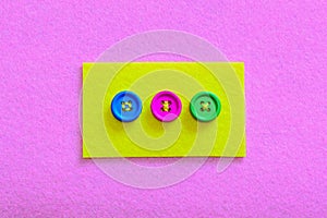 Easy ways to sew buttons to felt. Yellow felt piece with colourful buttons isolated on pink felt background