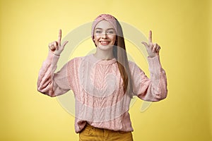 Easygoing beautiful young female student in knitted sweater, headband pointing up, promoting advertisement, smiling
