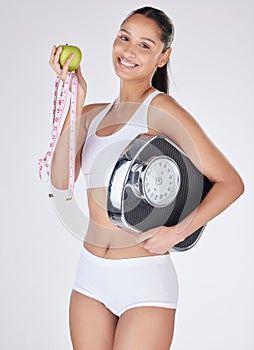 Eat healthy and exercise. Studio portrait of an attractive young woman eating an apple while holding a measuring tape