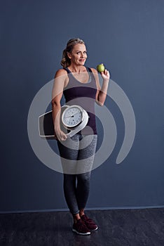 Eat right and exercise. Studio portrait of an attractive mature woman holding an apple and a weightscale against a blue