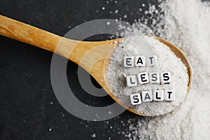 Eat less salt in order to reduce blood pressure or hypertension risk with sprinkled salt on dark background