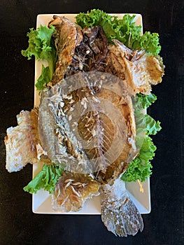 An eaten grilled snapper fish with bone and vegetable decorations on white plate in Thai seafood restaurant
