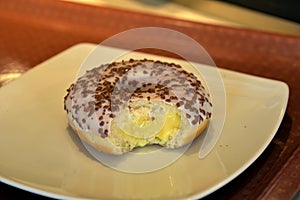 Vanilla cream filled doughnut with white crusting and chocolate on white ceramic plate photo