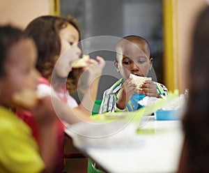 Eating, boy and children class for lunch at school or creche for an education or to learn. Break, kid and sandwich in a