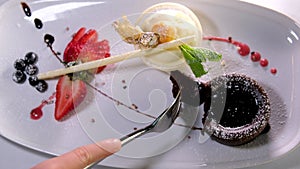 Eating brownie with fork. Taking bite of chocolate cake with chocolate icing and strawberries