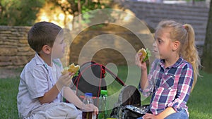 Eating children with sandwiches in their hands during lunch time and talk sitting on lawn in schoolyard