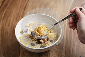 Eating corn flakes with fruits and nuts in white bowl