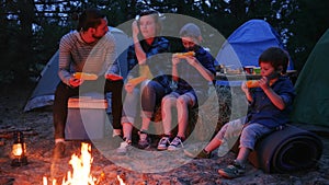 Eating dinner in evening near flames on nature, family enjoying corn with salt, picnic on outdoors, travel camp