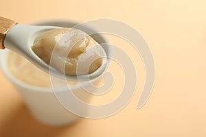 Eating healthy baby food with spoon on beige background, closeup. Space for text