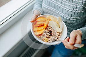 Eating healthy breakfast bowl muesli and fresh fruits in ceramic bowl in woman hands.
