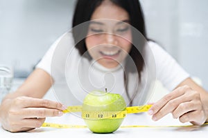 Eating healthy and dieting concept. Woman use measure tape measuring green apple on the table