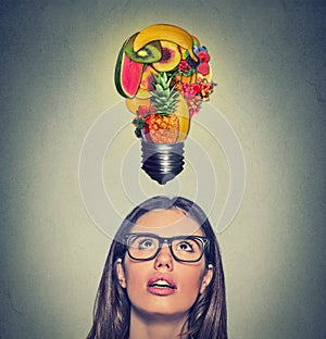 Eating healthy idea diet tips. Woman looking up light bulb made of fruits above head