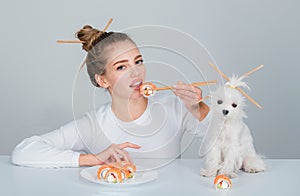 Eating japanese sushi set. Beauty young woman and dog eating sushi with a chopsticks, isolated on white. Sushi roll with