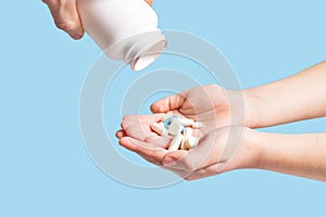 Eating a lot of drugs. Pills from plastic container. Tablets in hand on blue background