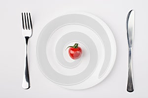 Eating a low calorie diet concept. Top above overhead flat-lay view photo of a plate with a single tomato with fork and knife