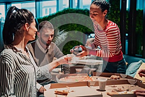 Eating pizza with diverse colleagues in the office, happy multi-ethnic employees having fun together during lunch