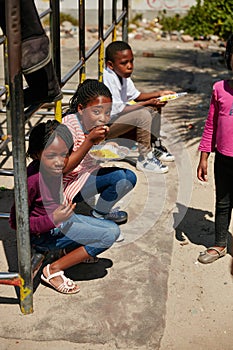 Eating on the playground. Full length portrait of children getting fed at a food outreach.