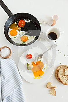 Eating in the process, fried eggs in a frying pan and on a plate, toast with avocado and a cup of coffee for breakfast.
