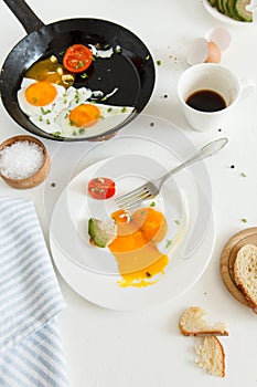 Eating in the process, fried eggs in a frying pan and on a plate, toast with avocado and a cup of coffee for breakfast.