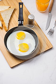 Eating in the process, fried eggs in a frying pan, toast and orange juice for breakfast on a white background. Daylight