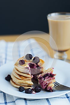 Eating of slapjack or oladyi with black raspberry with fork on white plate and cocoa