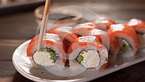 Eating Sushi with chopsticks. Philadelphia sushi roll japanese food in restaurant. Sushi roll with salmon, vegetables