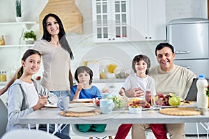 Eating together. Smiling hispanic parents spending time with their little children, having breakfast together at home