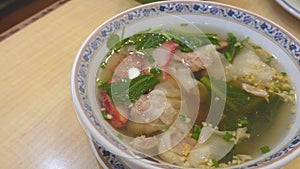 Eating Wonton Soup with BBQ Pork with spoon in white bowl. Wheat dough water dumplings stuffed with Shrimp and greens. prawn dumpl