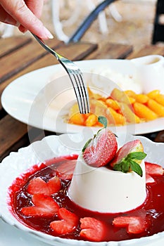 Eatting delicious italian dessert panna cotta with strawberry syrup