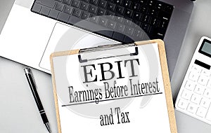 EBIT word on clipboard on laptop with calculator and pen
