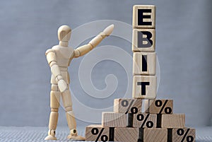 EBIT , the word is on cubes on a gray background, next to it is a wooden man
