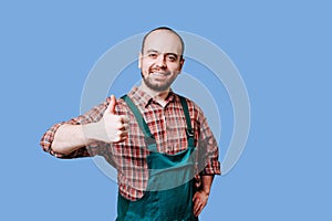 An ebullient young farmer with a beard is photographed in overalls, giving a thumb up