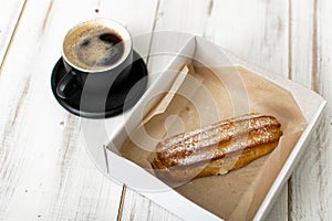 Eclair and coffee cup on a white wooden background
