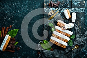 Eclair with cream. Creamy dessert on a black stone plate. Top view. Rustic style