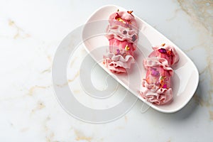 Eclair dessert with pink icing on white table close up