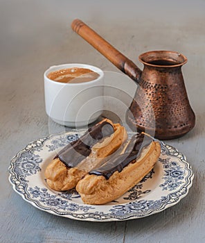 Eclairs, cezve and a cup of coffee on a gray background