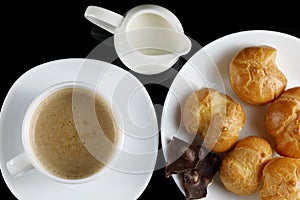 Eclairs with chocolate, cappuccino and milk. Sweet breakfast. Vanilla eclair and a cup of coffee