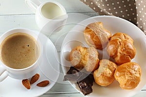 Eclairs with chocolate, cappuccino and milk. Sweet breakfast. Vanilla eclair and a cup of coffee