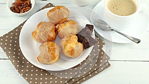 Eclairs with chocolate, cappuccino and milk. Sweet breakfast. Vanilla Ã©clair and a cup of coffee
