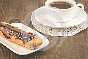 Eclairs with chocolate and a coffee cup/breakfast with eclairs with chocolate and a coffee cup on a wooden background. Selective