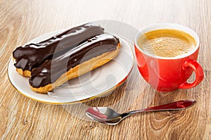 Eclairs with chocolate glaze in plate, cup with coffee, spoon on wooden plate