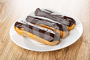 Eclairs with chocolate glaze in plate on wooden plate