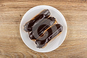 Eclairs with chocolate glaze in plate on wooden plate. Top view