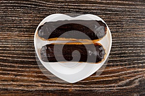 Eclairs with chocolate glaze in plate on wooden table. Top view