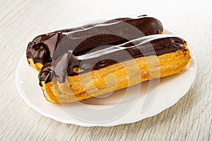 Eclairs with chocolate glaze in white plate on wooden table